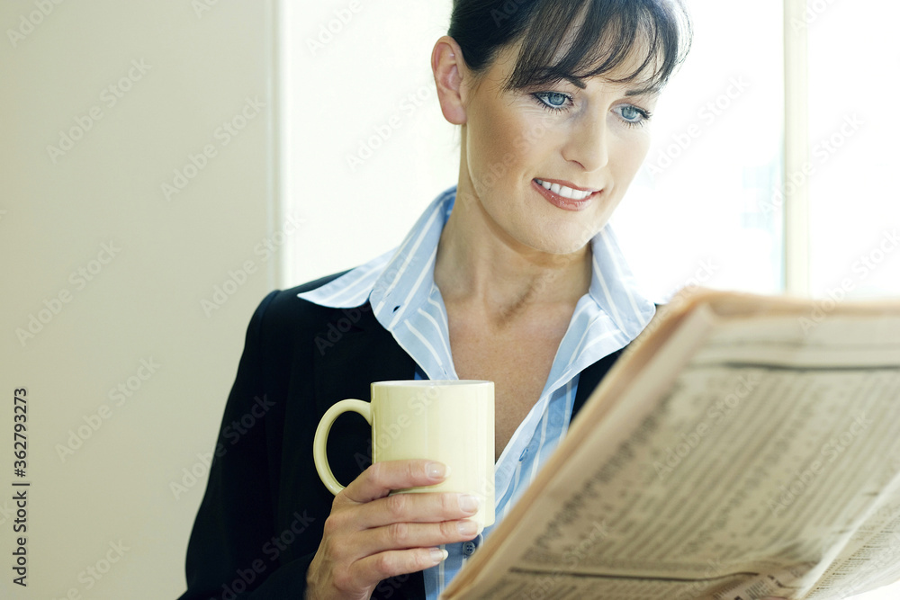 Businesswoman holding a cup of coffee while reading newspaper Businesswoman holding a cup of coffee while reading newspaper