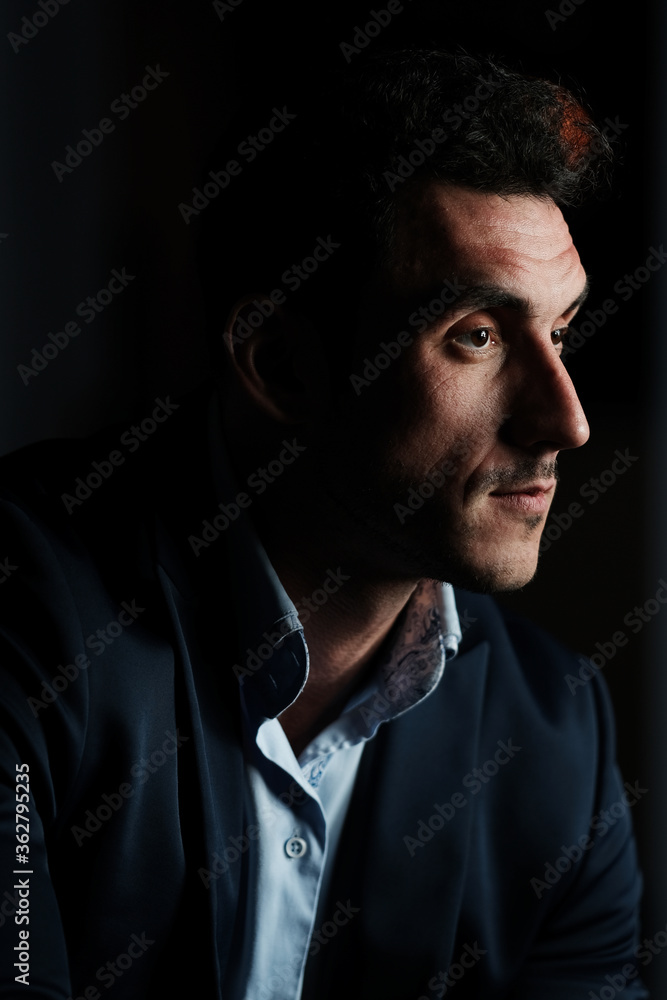 Fototapeta premium Close up portrait of a serious man 30-34 years old in a blue shirt and a dark jacket on a black background.