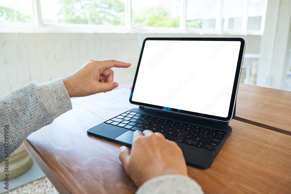 Mockup image of a woman using and pointing finger at tablet pc with blank desktop white screen as a computer pc on wooden table Mockup image of a woman using and pointing finger at tablet pc with blank desktop white screen as a computer pc on wooden table