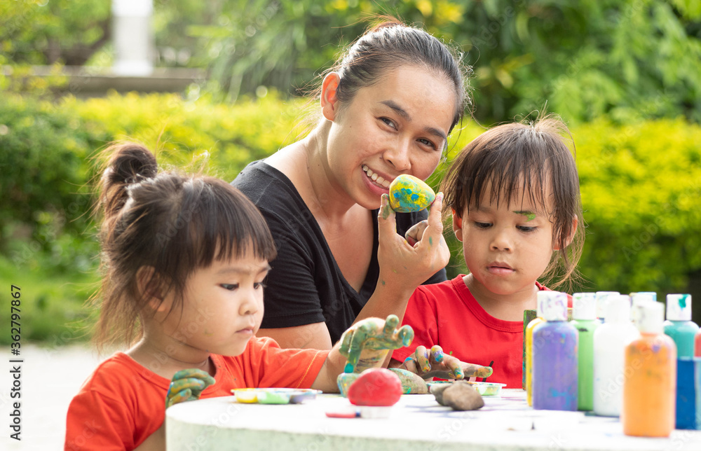 Asian two little sisters enjoy with hand-painted by acrylic paint on stones and wooden blocks with her mother on hot summer day. Children's creativity, crafts. Asian two little sisters enjoy with hand-painted by acrylic paint on stones and wooden blocks with her mother on hot summer day. Children's creativity, crafts.