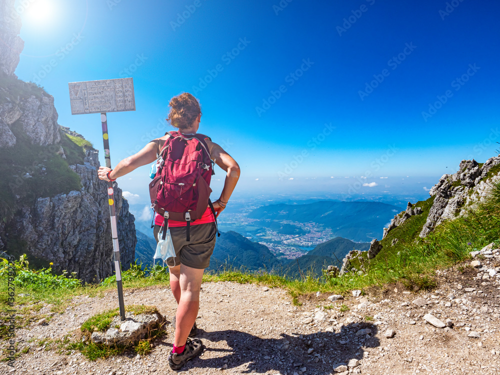 Woman admiring the landscape in the italian alps of Valsassina. On the sign are indicated the distances of the various trails