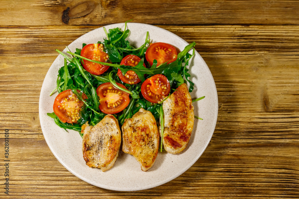 Fried chicken breast with salad of fresh arugula and cherry tomatoes on wooden table. Top view