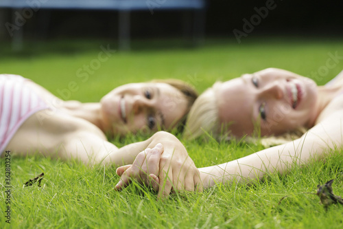 Teenage girls holding hands while lying on the field