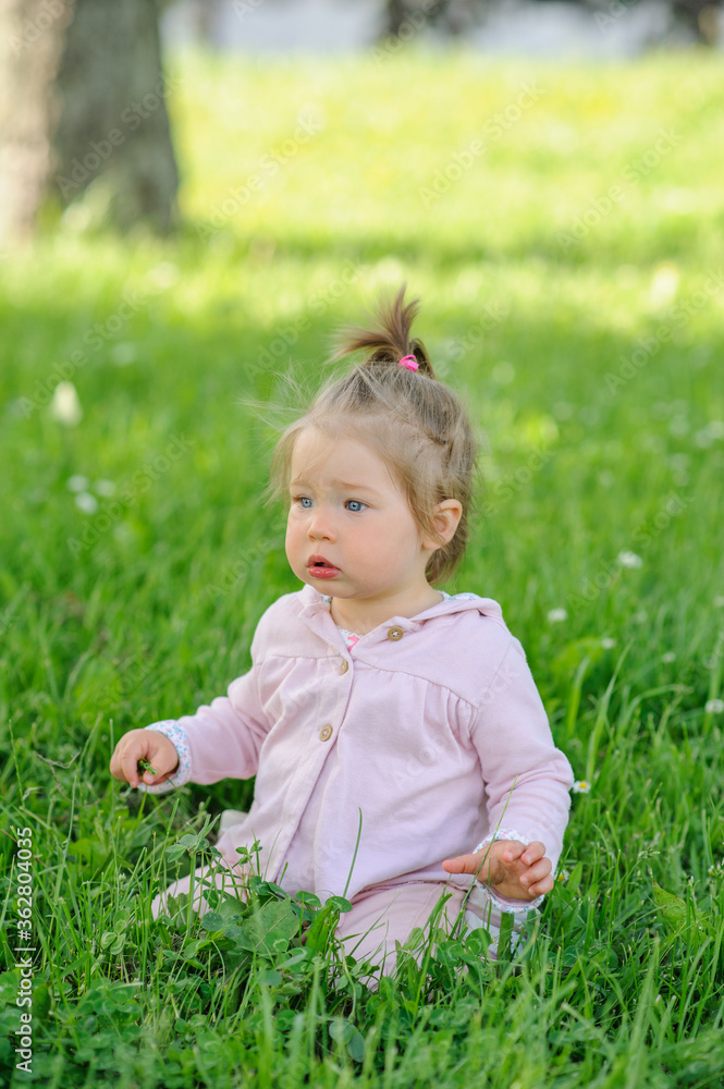 Little cute girl in casual wear sits on her knees on the green grass. Little cute girl in casual wear sits on her knees on the green grass.