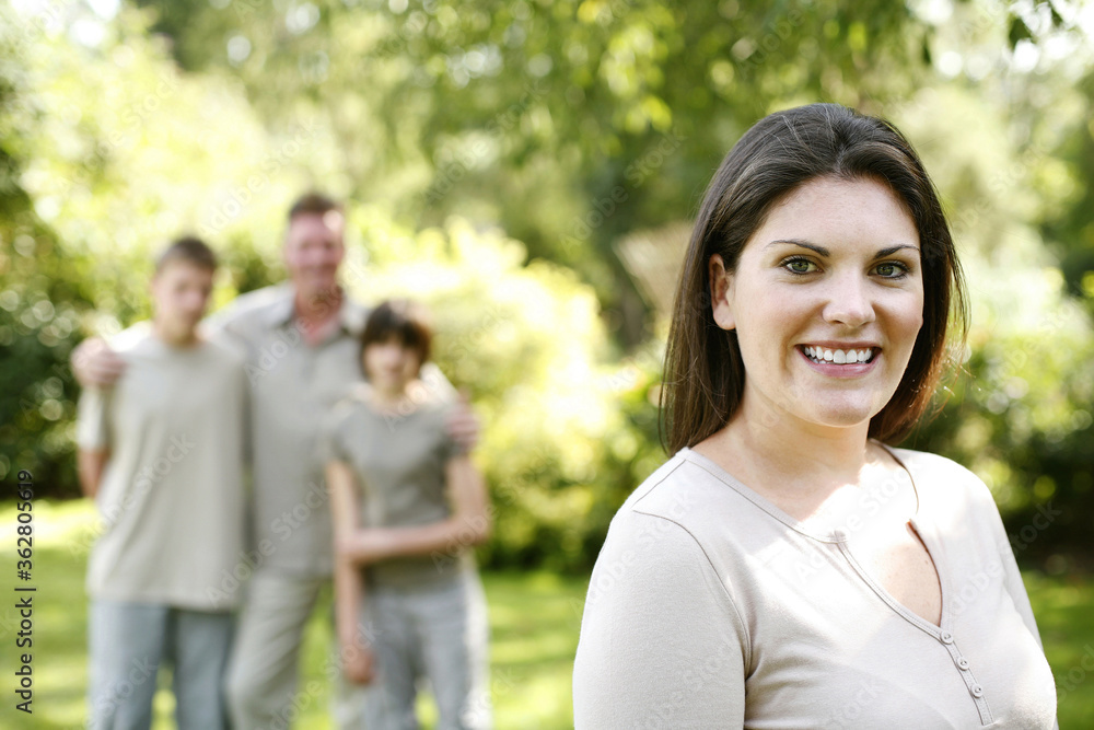 Woman smiling at the camera with her family standing in the background Woman smiling at the camera with her family standing in the background