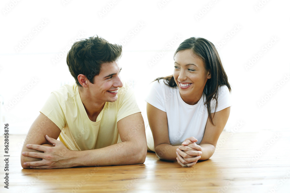 Couple lying forward on the floor smiling at each other Couple lying forward on the floor smiling at each other