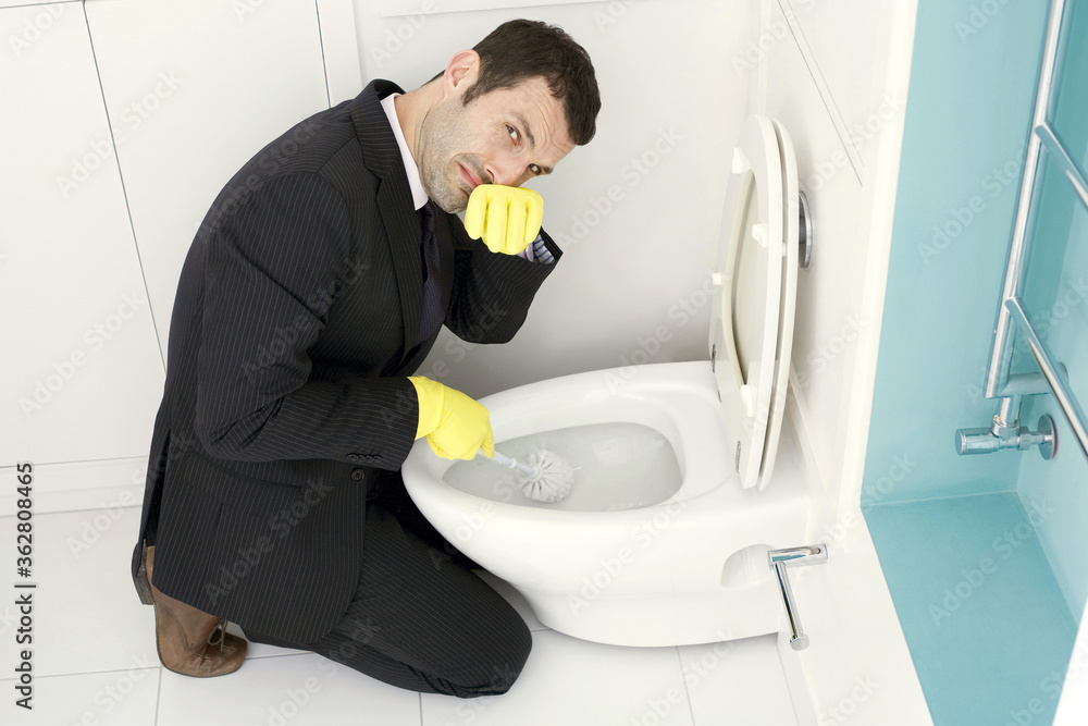 Businessman cleaning the toilet bowl, pulling face Businessman cleaning the toilet bowl, pulling face