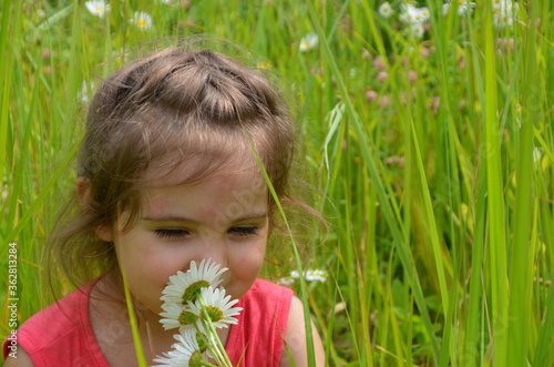 outdoor portrait Cute smiling baby girl in camomile field .Adorable girl with blue eyes and flowers daisies on meadow at summer day.Little child having fun and exploring nature. Copy space