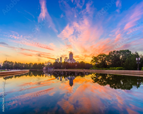 Dawn over Victory Park on Poklonnaya Hill in Moscow in the summer. Colorful blue sky with clouds and sunrise on the horizon above an Orthodox church. The sky is reflected in the pool of the fountain.