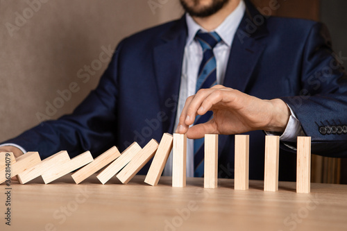 Businessman hand Stopping Falling wooden Dominoes effect from continuous toppled or risk, strategy and successful intervention concept for business.