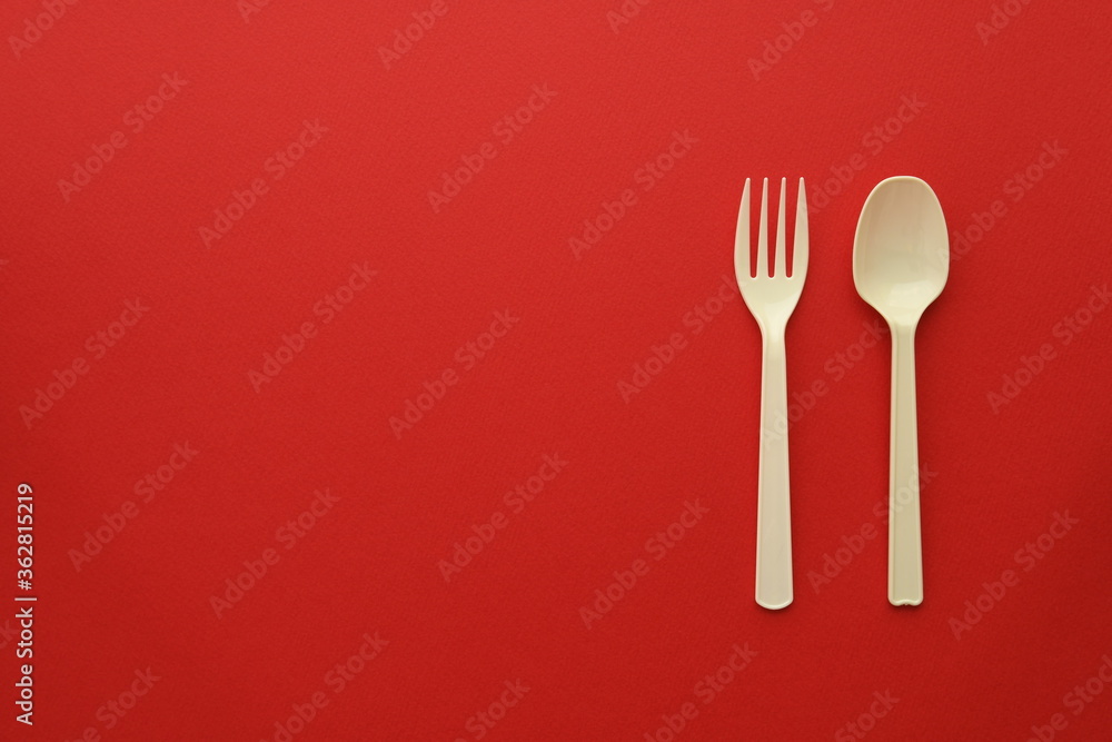Plastic disposable fork and spoon on red background Plastic disposable fork and spoon on red background