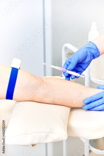  doctor takes a test from a vein with a syringe. medical tourniquet is placed on the man’s arm