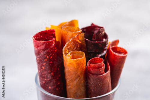 Fruit pastille in glass cup on stone concrete background. Organic sugar free roll up food made from raspberry, strawberry, peach and apple. Vegan homemade sweets. Angle view macro