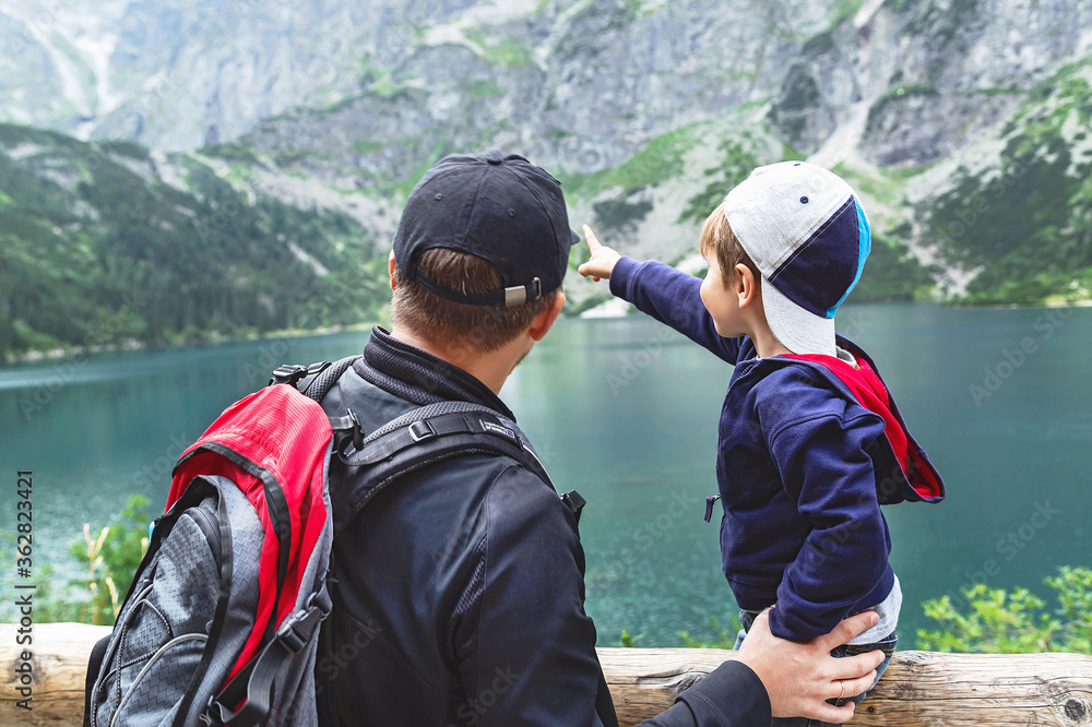 Father and his son near the Eye of the Sea lake in Tatra mountains. Happy enthusiastic boy is pointing to the mountains. Father and his son near the Eye of the Sea lake in Tatra mountains. Happy enthusiastic boy is pointing to the mountains.