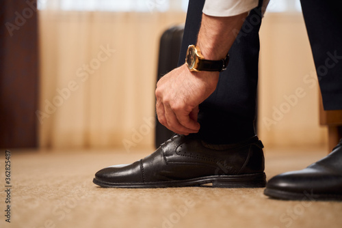 Man with classic watch tying shoelaces indoors