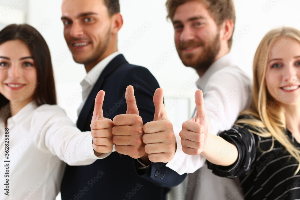 Happy successful young men and women looking at camera and standing in the office together with thumbs up Happy successful young men and women looking at camera and standing in the office together with thumbs up