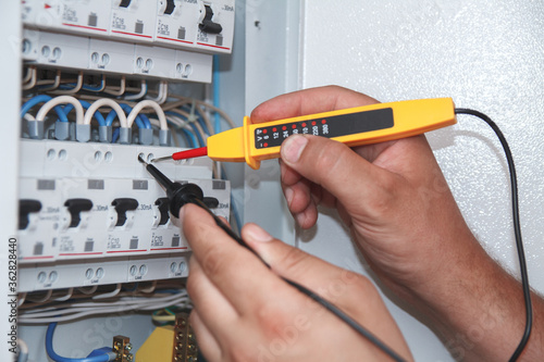 Electrician with multimeter probe at an electrical switchgear ca
