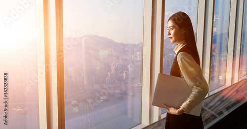 Successful female office worker with net-book is standing in skyscraper interior against big window with city view on background. Proud asian woman architect looking satisfied with completed project Free Download Successful female office worker with net-book is standing in skyscraper interior against big window with city view on background. Proud asian woman architect looking satisfied with completed project - GFXLoad