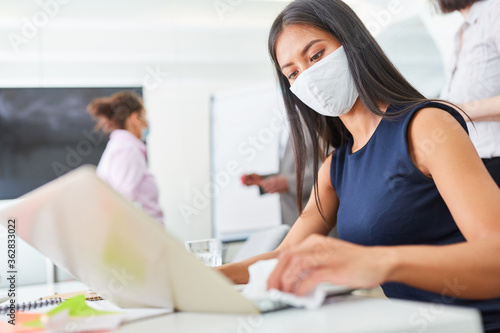 Geschäftsfrau mit Gesichtsmaske beim Tastatur desinfizieren