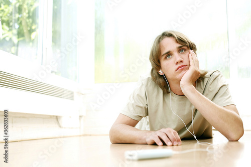 Teenage boy lying forward on the floor listening to music on portable music player