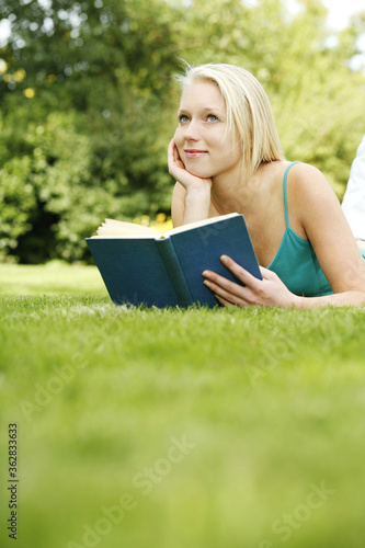 Teenage girl lying forward on the field holding book © ImageHit