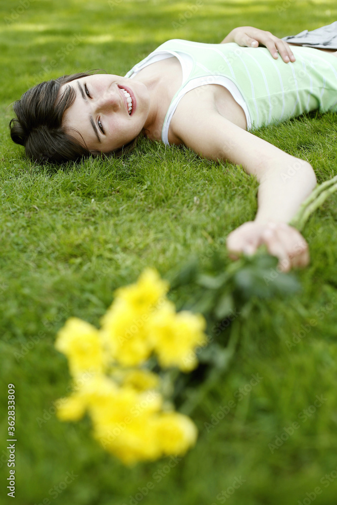 Teenage girl lying down on the field with yellow flowers in her hand Teenage girl lying down on the field with yellow flowers in her hand