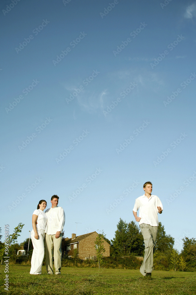 Teenage boy jogging with his parents watching Teenage boy jogging with his parents watching