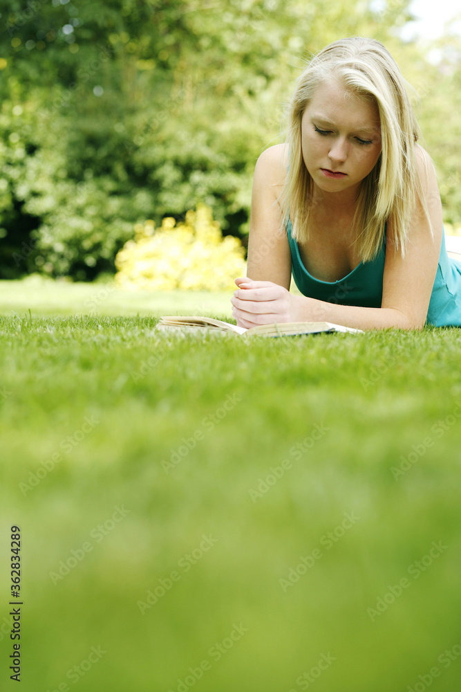 Teenage girl lying forward on the field reading book Teenage girl lying forward on the field reading book