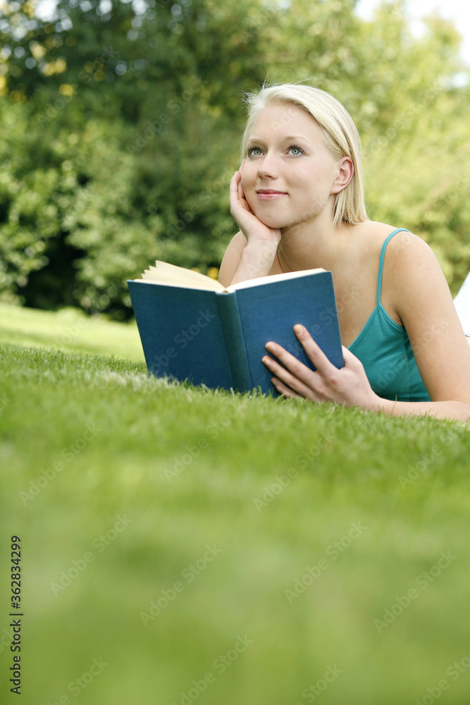 Teenage girl lying forward on the field holding book Teenage girl lying forward on the field holding book