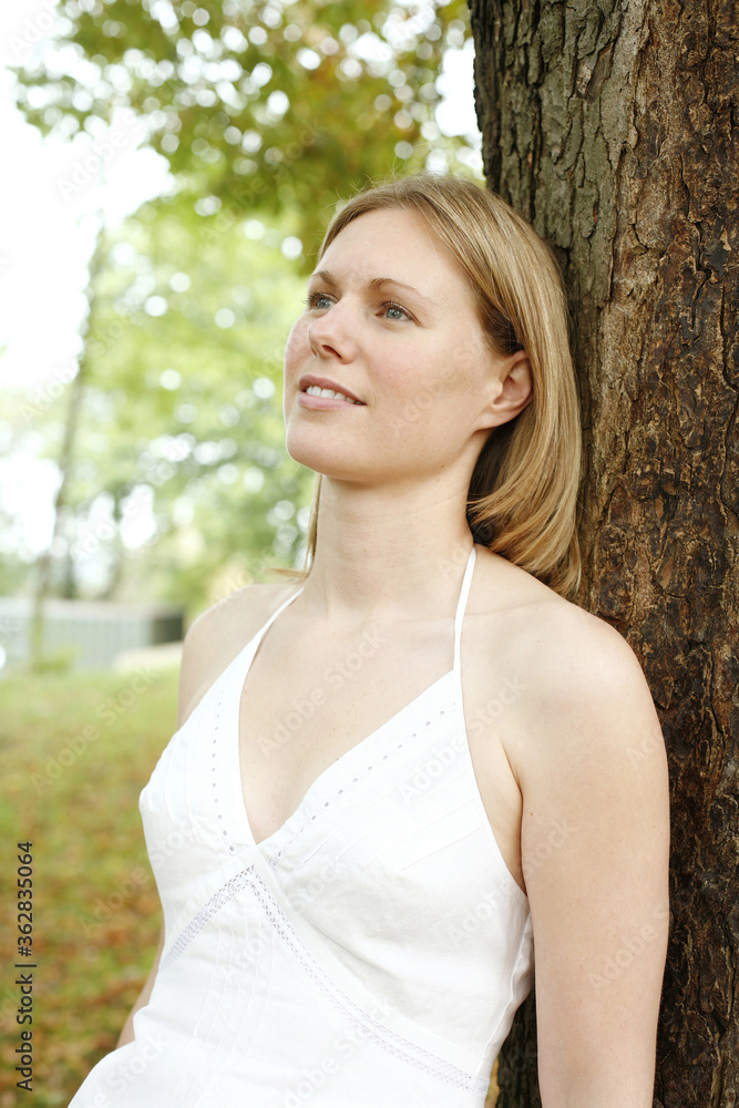 Woman leaning against a tree while daydreaming Woman leaning against a tree while daydreaming