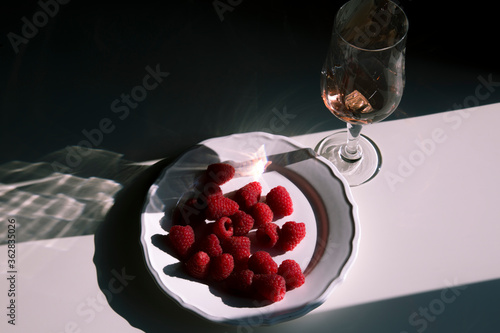 raspberries on a white plate and wine on a romantic modern background in summer style, concept for a food blog, beautiful shadow