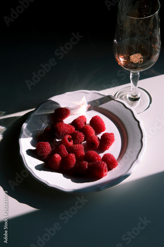 raspberries on a white plate and wine on a romantic modern background in summer style, concept for a food blog, beautiful shadow