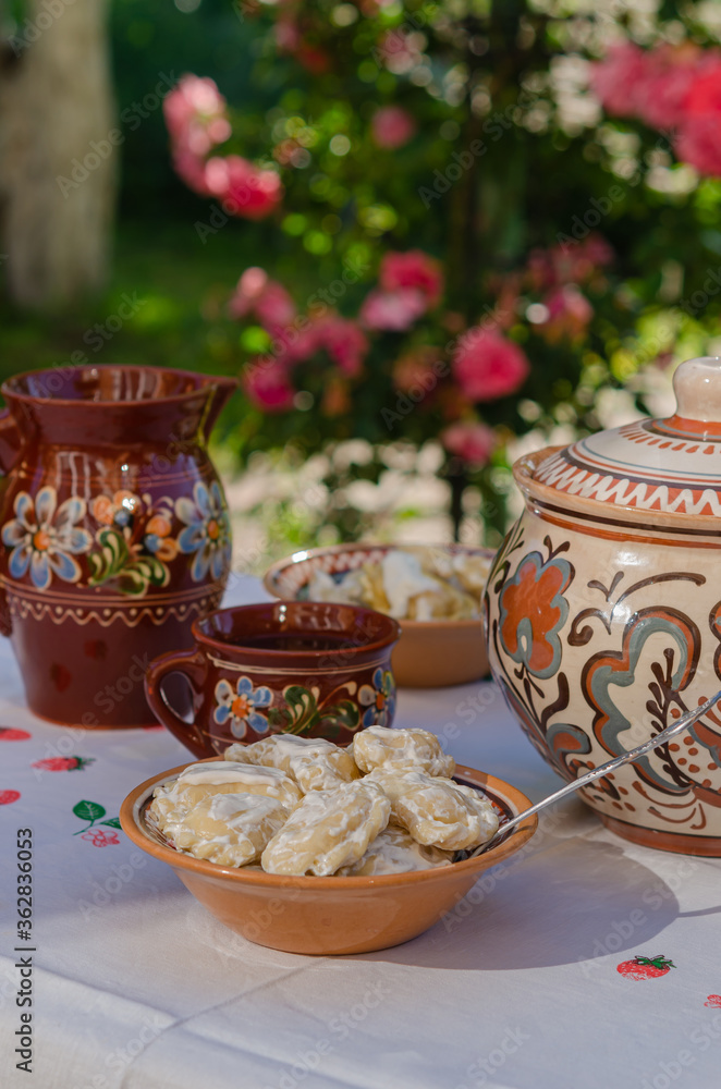 Homemade pierogi in clay ethnic Ukrainian dishes on a table in the summer garden.