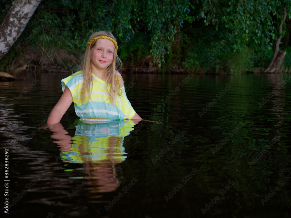 Fototapeta premium blonde girls with blue eyes bathes in clothes in the dark water of a lake at sunset