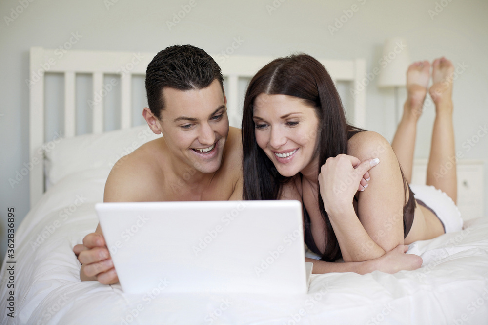 Couple lying forward on the bed using laptop Couple lying forward on the bed using laptop