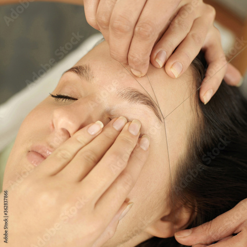 Hand using thread to remove facial hair from woman's face