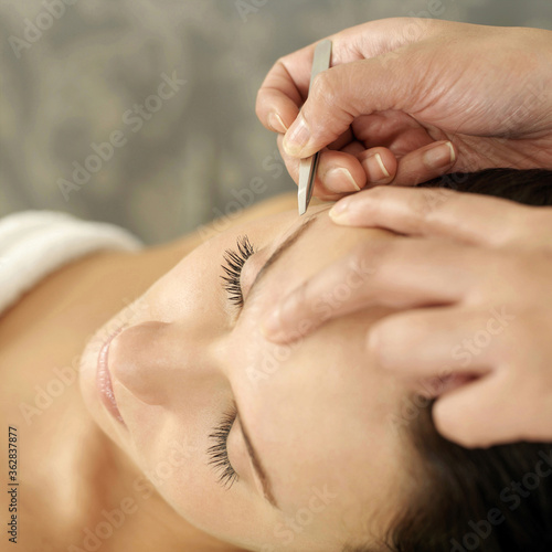 Hand tweezing woman's eyebrow