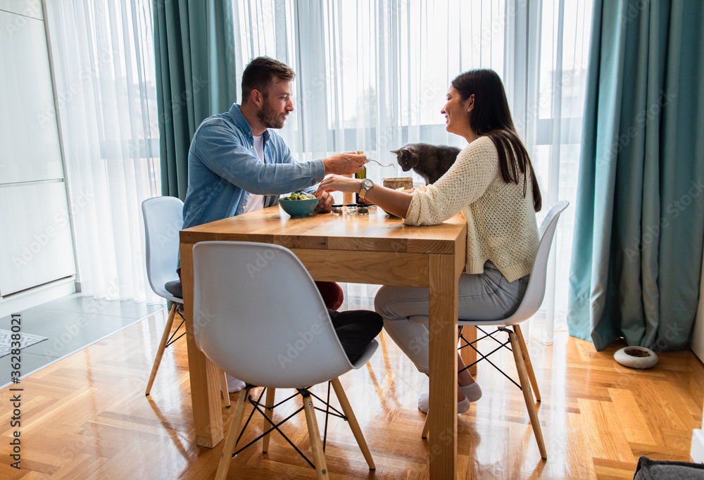 Young couple eating salad while sitting at a table at home. Young couple eating salad while sitting at a table at home.