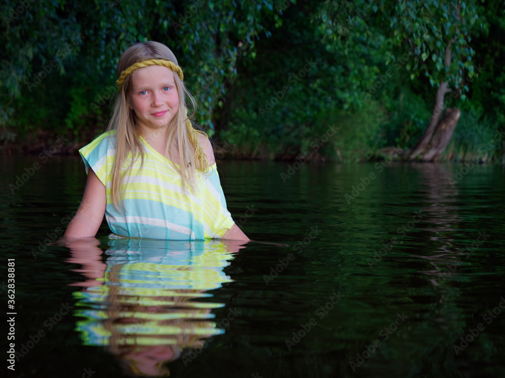 Fototapeta premium blonde girls with blue eyes bathes in clothes in the dark water of a lake at sunset