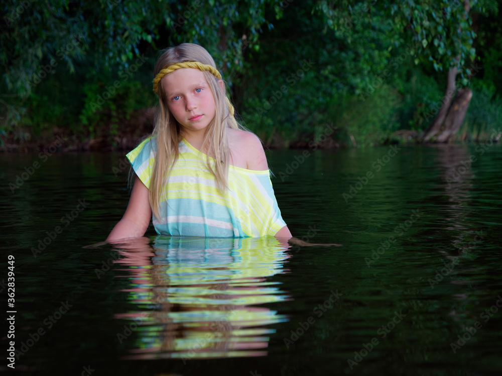 Fototapeta premium blonde girls with blue eyes bathes in clothes in the dark water of a lake at sunset