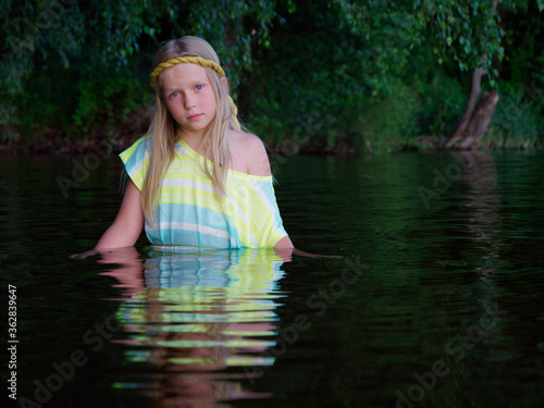 Fototapeta Naklejka Na Ścianę i Meble -  blonde girls with blue eyes bathes in clothes in the dark water of a lake at sunset