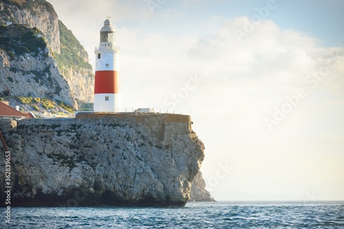 Trinity lighthouse at the rocky shore (cliffs) of the Europa Point. British Overseas Territory of Gibraltar, Mediterranean sea. National landmark, sightseeing, travel destination, famous place, travel
