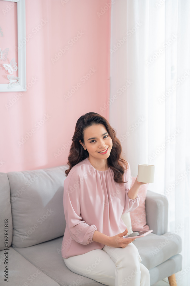 Attractive young Asian woman using phone and drinking coffee when sitting on sofa at home. Attractive young Asian woman using phone and drinking coffee when sitting on sofa at home.