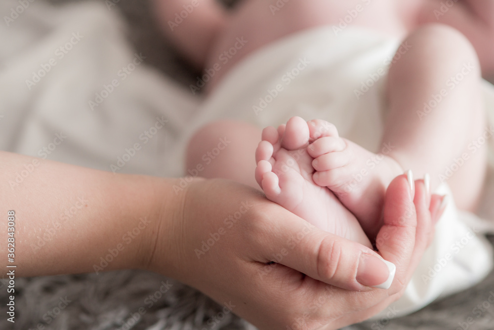 Maternal hands hold baby legs on the bed at home. Happy and healthy motherhood. Child care Maternal hands hold baby legs on the bed at home. Happy and healthy motherhood. Child care