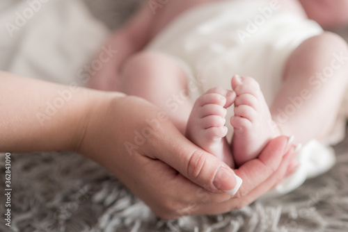 Maternal hands hold baby legs on the bed at home. Happy and healthy motherhood. Child care