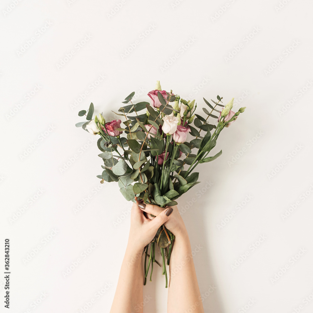 Female hands holding colorful roses flowers bouquet against white wall. Holiday celebration festive floral concept