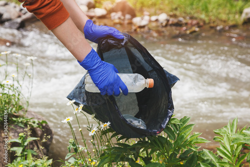 volunteer young woman collecting garbage and picking up plastic bottle waste at dirty nature, earth and water pollution