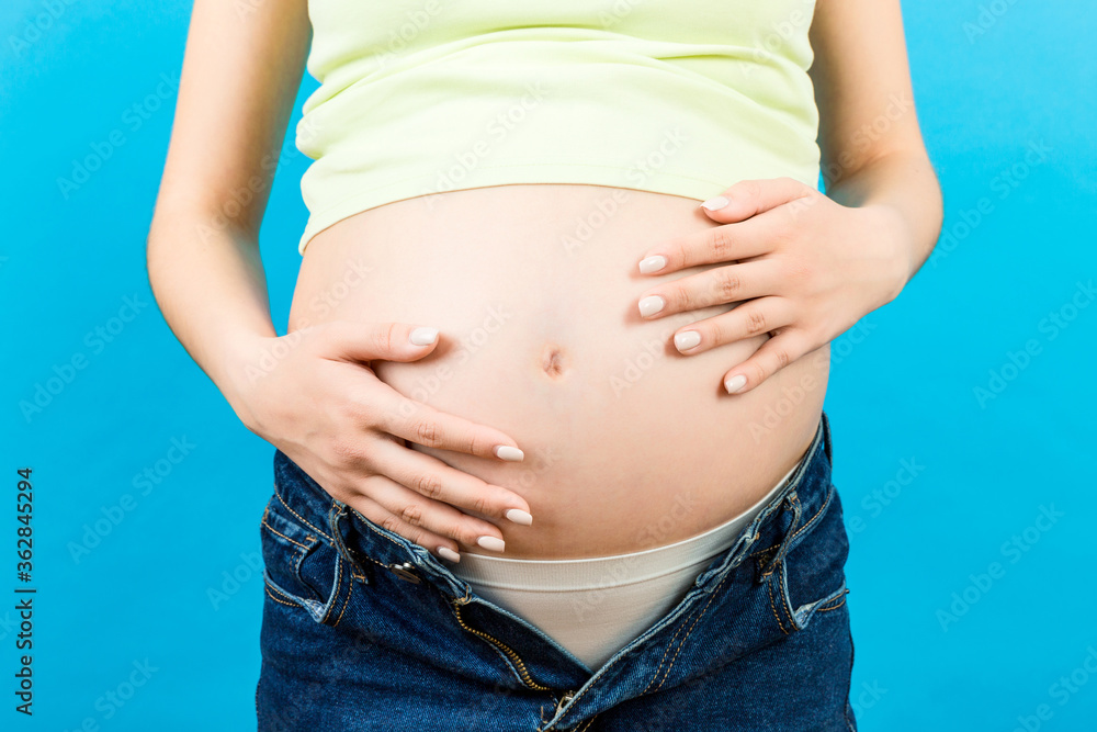 Close up of expecting mother in unzipped jeans showing her naked pregnant belly at colorful background with copy space. Pregnancy concept Close up of expecting mother in unzipped jeans showing her naked pregnant belly at colorful background with copy space. Pregnancy concept
