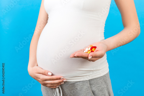 Close up of pregnant woman holding a stack of vitamin pills in her hand at colorful background with copy space. Medicine concept