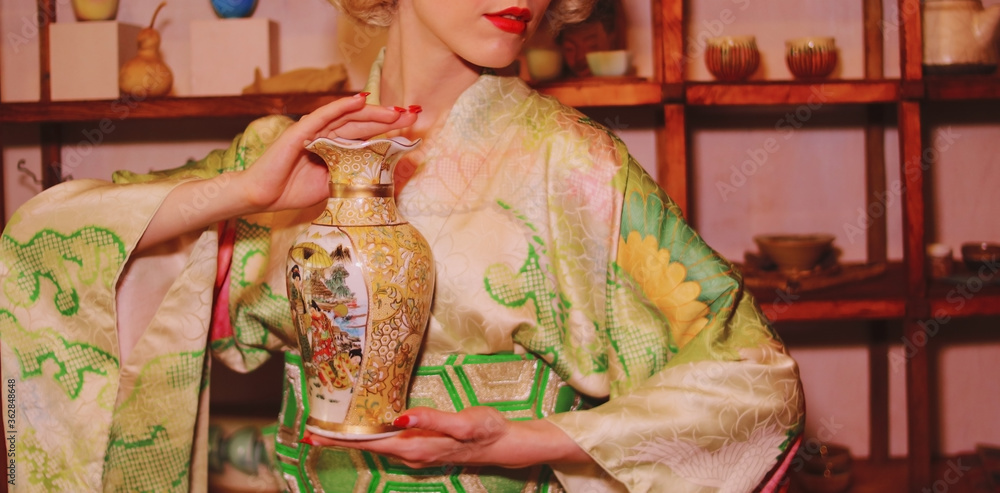 A girl in a green kimono holds in her hands an old golden Chinese vase A girl in a green kimono holds in her hands an old golden Chinese vase